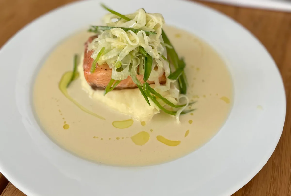 Stekt laxbit på potatispuré med fänkålssallad och krämig sås på vit tallrik